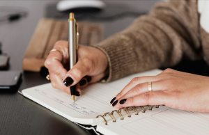 Woman's hands writing in a notebook with a pen.